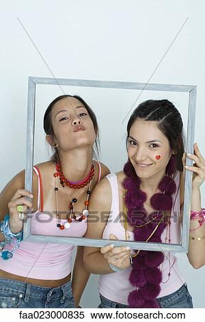 Two young female friends holding up picture frame, smiling and puckering at camera, portrait View Large Photo Image Stock Photography - Two young female friends holding up picture frame, smiling and puckering at camera, portrait. Fotosearch