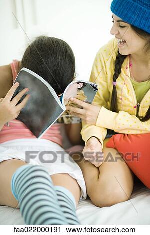 Two young female friends looking in magazine together, laughing, one hiding face in magazine View Large Photo Image Stock Image - Two young female friends looking in magazine together, laughing, one hiding face in magazine. Fotosearch