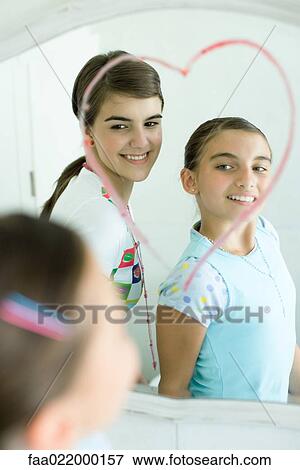 Two young female friends looking in mirror, heart drawn on mirror with lipstick View Large Photo Image Stock Photo - Two young female friends looking in mirror, heart drawn on mirror with lipstick. Fotosearch