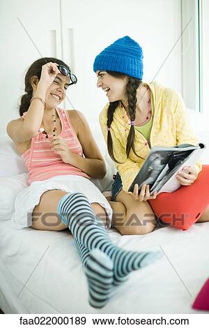 Two young female friends looking in magazine together, laughing View Large Photo Image Stock Photo - Two young female friends looking in magazine together, laughing. Fotosearch