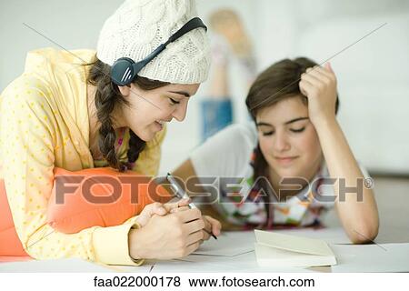Two young female friends lying on floor, doing homework together View Large Photo Image Stock Photo - Two young female friends lying on floor, doing homework together. Fotosearch