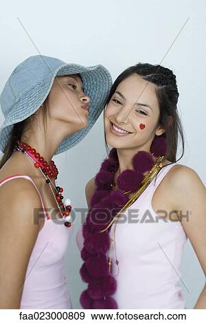 Stock Photo - Two young female friends, one about to kiss the other's cheek, portrait. Fotosearch