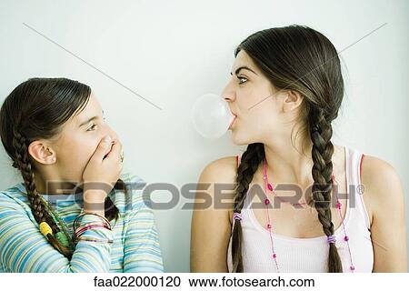 Two young female friends, one blowing bubble while other watches and covers mouth View Large Photo Image Stock Image - Two young female friends, one blowing bubble while other watches and covers mouth. Fotosearch