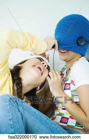 Stock Image - Two young female friends, one hiding face under hat, other pulling up hat. Fotosearch