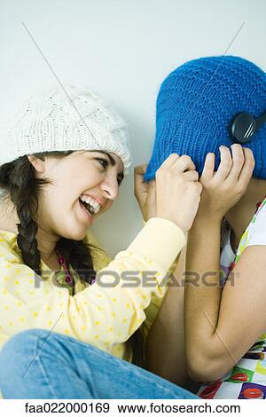 Stock Photo - Two young female friends, one hiding face under hat. Fotosearch