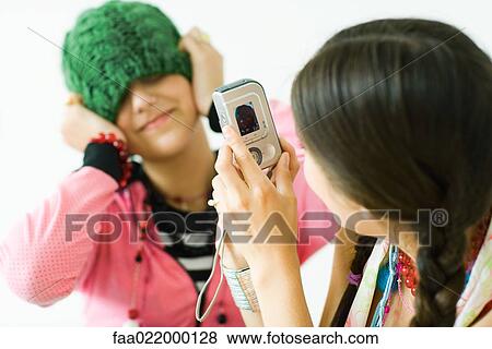 Two young female friends, one taking photo of the other View Large Photo Image Stock Photo - Two young female friends, one taking photo of the other. Fotosearch