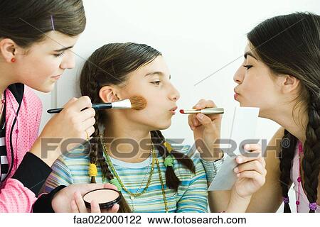 Two young female friends putting make-up on younger girl View Large Photo Image Stock Image - Two young female friends putting make-up on younger girl. Fotosearch