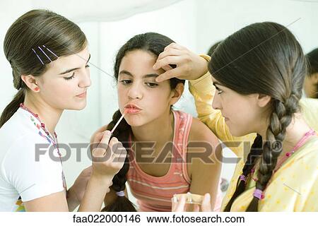 Two young female friends putting make-up on younger girl View Large Photo Image Stock Photograph - Two young female friends putting make-up on younger girl. Fotosearch