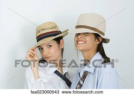 Stock Image - Two young female friends wearing hats and ties, smiling at camera, portrait. Fotosearch