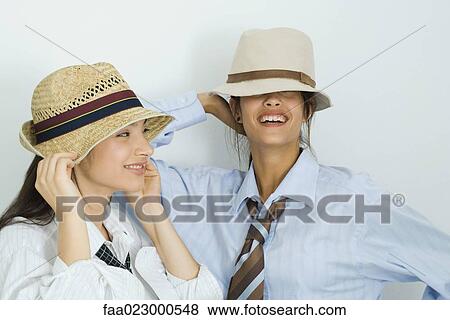 Two young female friends wearing hats, smiling, one's eyes covered View Large Photo Image Stock Photo - Two young female friends wearing hats, smiling, one's eyes covered. Fotosearch
