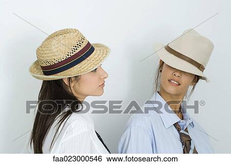 Two young female friends wearing hats and ties, looking at each other, one's eyes covered View Large Photo Image Stock Photograph - Two young female friends wearing hats and ties, looking at each other, one's eyes covered. Fotosearch
