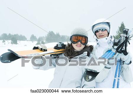 Two young friends carrying skis on shoulders, smiling at camera View Large Photo Image Picture - Two young friends carrying skis on shoulders, smiling at camera. Fotosearch