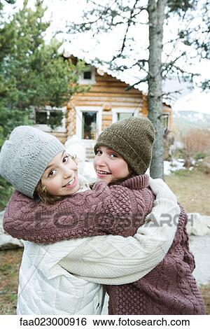 Two young friends embracing, dressed in winter clothing, looking over shoulders at camera View Large Photo Image Stock Photograph - Two young friends embracing, dressed in winter clothing, looking over shoulders at camera. Fotosearch