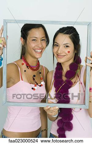 Two young friends holding up frame together, smiling at camera, portrait View Large Photo Image Picture - Two young friends holding up frame together, smiling at camera, portrait. Fotosearch