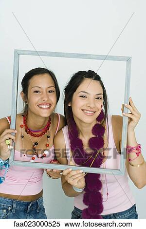 Two young friends holding up frame together, smiling at camera, portrait View Large Photo Image Stock Photography - Two young friends holding up frame together, smiling at camera, portrait. Fotosearch