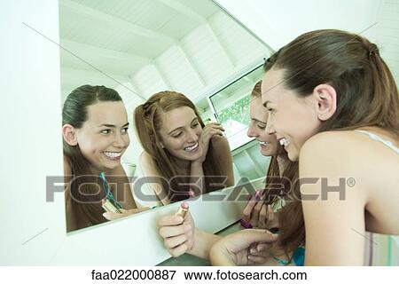Two young friends lying on ground, looking at selves in mirror, holding lipstick View Large Photo Image Stock Photo - Two young friends lying on ground, looking at selves in mirror, holding lipstick. Fotosearch