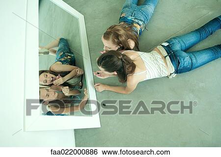 Two young friends lying on ground, looking at selves in mirror, holding lipstick, view from directly above View Large Photo Image Stock Photograph - Two young friends lying on ground, looking at selves in mirror, holding lipstick, view from directly above. Fotosearch