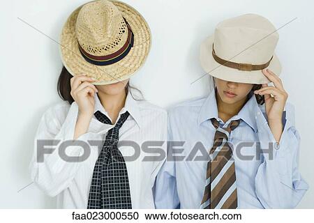 Two young friends pulling hats down over their faces, portrait View Large Photo Image Stock Image - Two young friends pulling hats down over their faces, portrait. Fotosearch