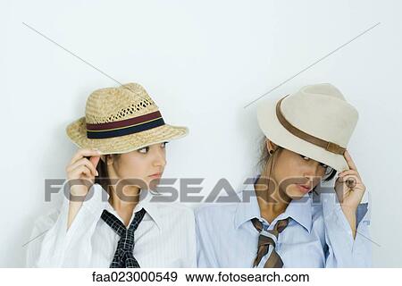 Two young friends pulling hats down over their faces, one looking at camera, portrait View Large Photo Image Stock Photo - Two young friends pulling hats down over their faces, one looking at camera, portrait. Fotosearch