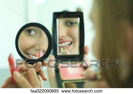 Two young friends putting on lipstick, looking at selves in hand mirrors, cropped view View Large Photo Image Stock Photography - Two young friends putting on lipstick, looking at selves in hand mirrors, cropped view. Fotosearch
