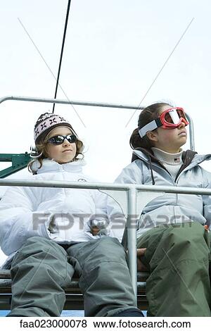 Two young friends sitting on chair lift, side by side, looking away View Large Photo Image Stock Photo - Two young friends sitting on chair lift, side by side, looking away. Fotosearch