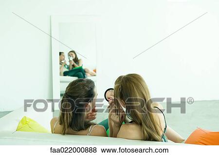 Two young friends sitting side by side, looking in hand mirror, putting on lipstick, rear view View Large Photo Image Stock Photo - Two young friends sitting side by side, looking in hand mirror, putting on lipstick, rear view. Fotosearch