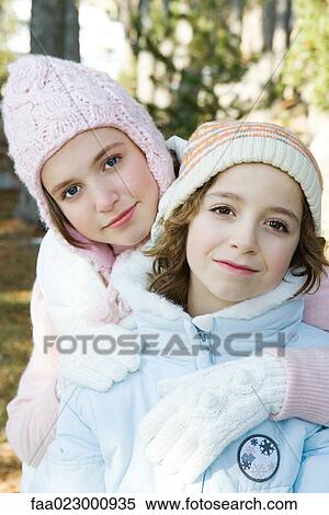 Stock Photography - Two young friends smiling at camera, wearing knit hats, one's arm around the other's shoulder, portrait. Fotosearch