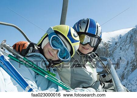 Two young skiers on chair lift, smiling at camera together, portrait View Large Photo Image Stock Photograph - Two young skiers on chair lift, smiling at camera together, portrait. Fotosearch