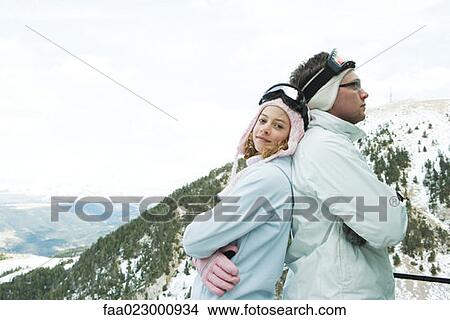 Picture - Two young skiers standing back to back, smiling, one looking at camera, portrait. Fotosearch