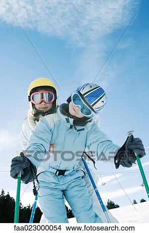 Two young skiers standing, one behind the other, both smiling at camera, low angle view View Large Photo Image Picture - Two young skiers standing, one behind the other, both smiling at camera, low angle view. Fotosearch