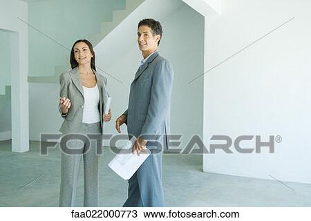 Well dressed man and woman standing in bare home interior, woman holding binder, man holding blueprints View Large Photo Image Stock Image - Well dressed man and woman standing in bare home interior, woman holding binder, man holding blueprints. Fotosearch