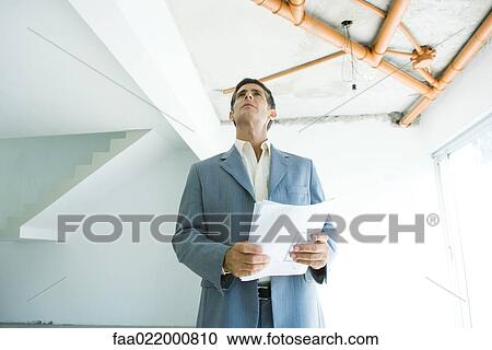 Well-dressed man holding blueprints, inspecting unfinished home interior View Large Photo Image Stock Image - Well-dressed man holding blueprints, inspecting unfinished home interior. Fotosearch