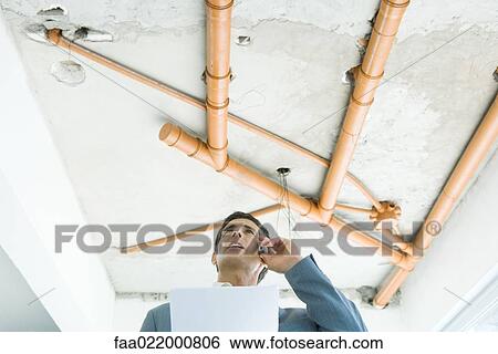 Stock Photograph - Well-dressed man using phone, inspecting unfinished home interior. Fotosearch