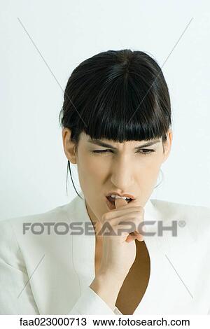 Stock Image - Well-dressed young businesswoman biting thumb, portrait. Fotosearch