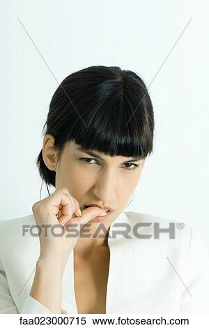 Stock Photography - Well-dressed young businesswoman biting thumb, looking at camera, portrait. Fotosearch