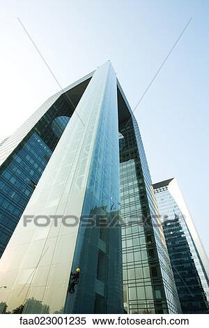 Stock Photography - Window washer on corner of skyscraper, low angle view. Fotosearch