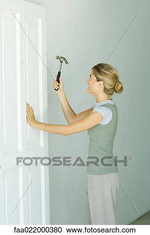 Woman hammering nail into door View Large Photo Image Stock Image - Woman hammering nail into door. Fotosearch