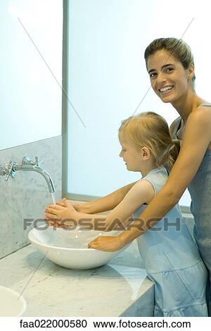 Woman helping little girl wash hands in bathroom sink, woman smiling at camera View Large Photo Image Stock Image - Woman helping little girl wash hands in bathroom sink, woman smiling at camera. Fotosearch