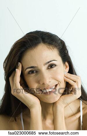 Stock Photography - Woman holding face between hands, smiling at camera, portrait. Fotosearch