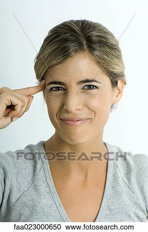 Stock Image - Woman holding finger to temple, making face, portrait. Fotosearch