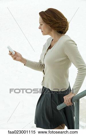 Woman holding railing, looking down at cell phone View Large Photo Image Stock Photography - Woman holding railing, looking down at cell phone. Fotosearch