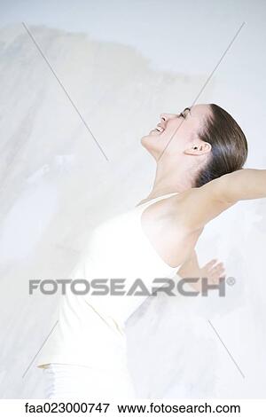 Stock Photo - Woman leaning back, arms outstretched, smiling, side view. Fotosearch