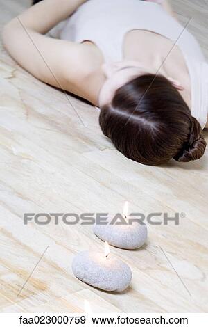 Stock Photo - Woman lying on back on the floor, burning candles in foreground. Fotosearch