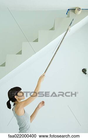 Stock Image - Woman painting ceiling with roller extension. Fotosearch