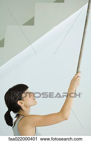Stock Image - Woman painting ceiling with roller extension. Fotosearch