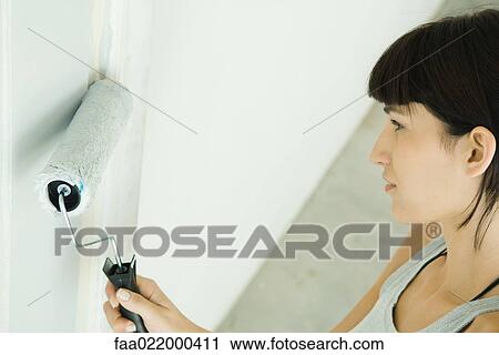 Stock Image - Woman painting door with paint roller. Fotosearch