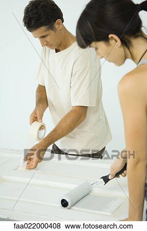 Stock Photo - Woman painting door with paint roller, man protecting woodwork with masking tape. Fotosearch