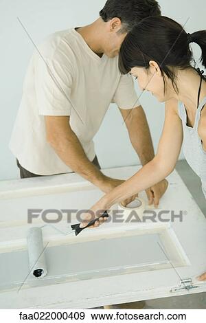 Stock Photo - Woman painting door with paint roller, man protecting woodwork with masking tape. Fotosearch