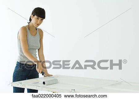 Stock Photography - Woman painting door with paint roller. Fotosearch