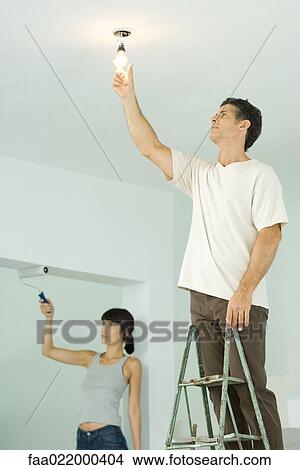 Picture - Woman painting with paint roller, man changing light bulb. Fotosearch